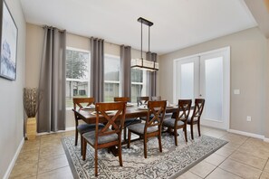 A dining area with a table set for six, six wooden chairs with cushioned seats, a patterned rug, and a pendant light. - The Magic Haven - 5BR - Sleeps 13 - Near Disney (Davenport)