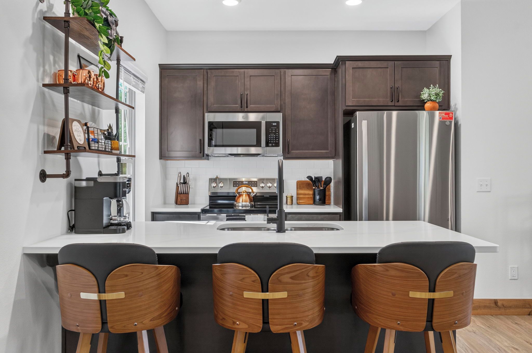 A modern kitchen with dark cabinets, stainless steel appliances, a central island with bar stools, and a coffee machine.