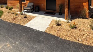 A wooden cabin with a black door, a small porch, and a chair. - NewCabin, Pools, Lazy River, Private HotTub, Firepit, near Branson, BigCedar (Hollister)