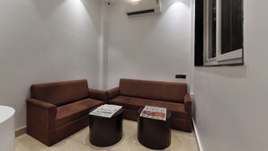 Una habitación moderna y minimalista con un sofá seccional marrón, dos mesitas redondas y un equipo de aire acondicionado instalado en el techo.