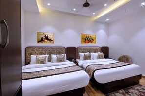 Quarto de hotel com duas camas, cada uma com cabeceiras estampadas e roupa de cama branca. Há duas pinturas penduradas na parede acima das camas.