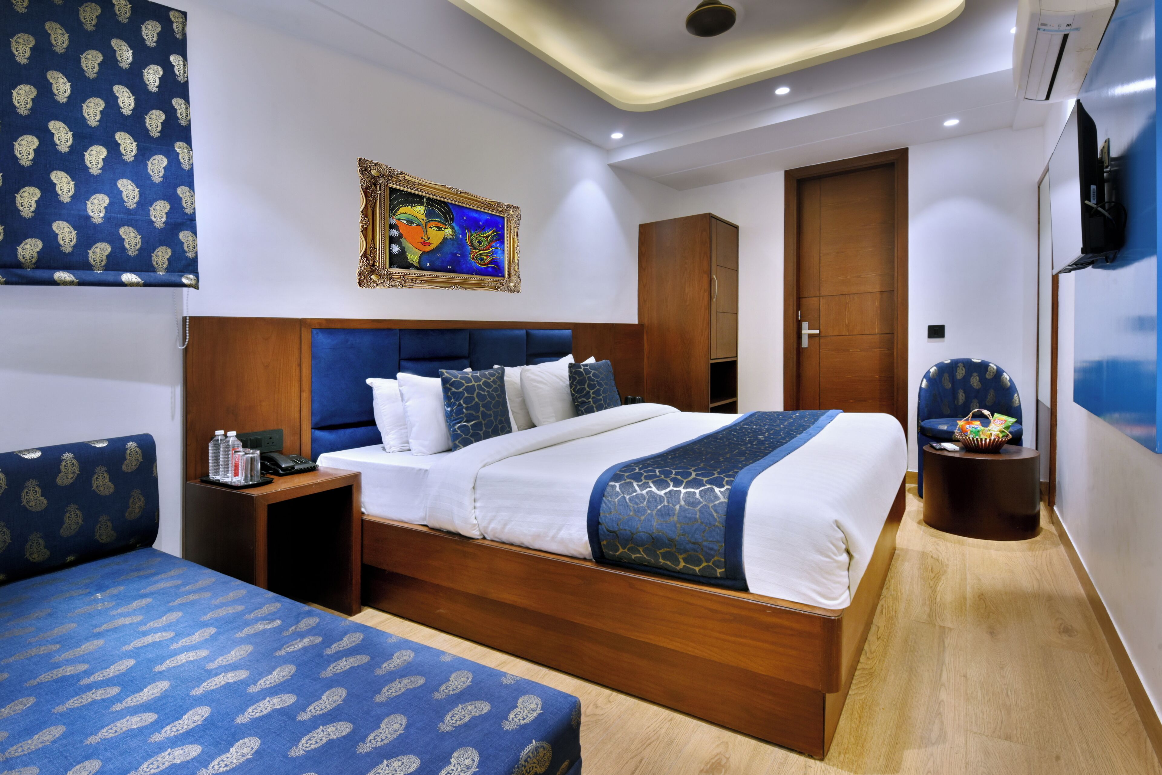 Une chambre d’hôtel avec un grand lit, une table de chevet, une armoire, un coin salon et un tableau au mur.