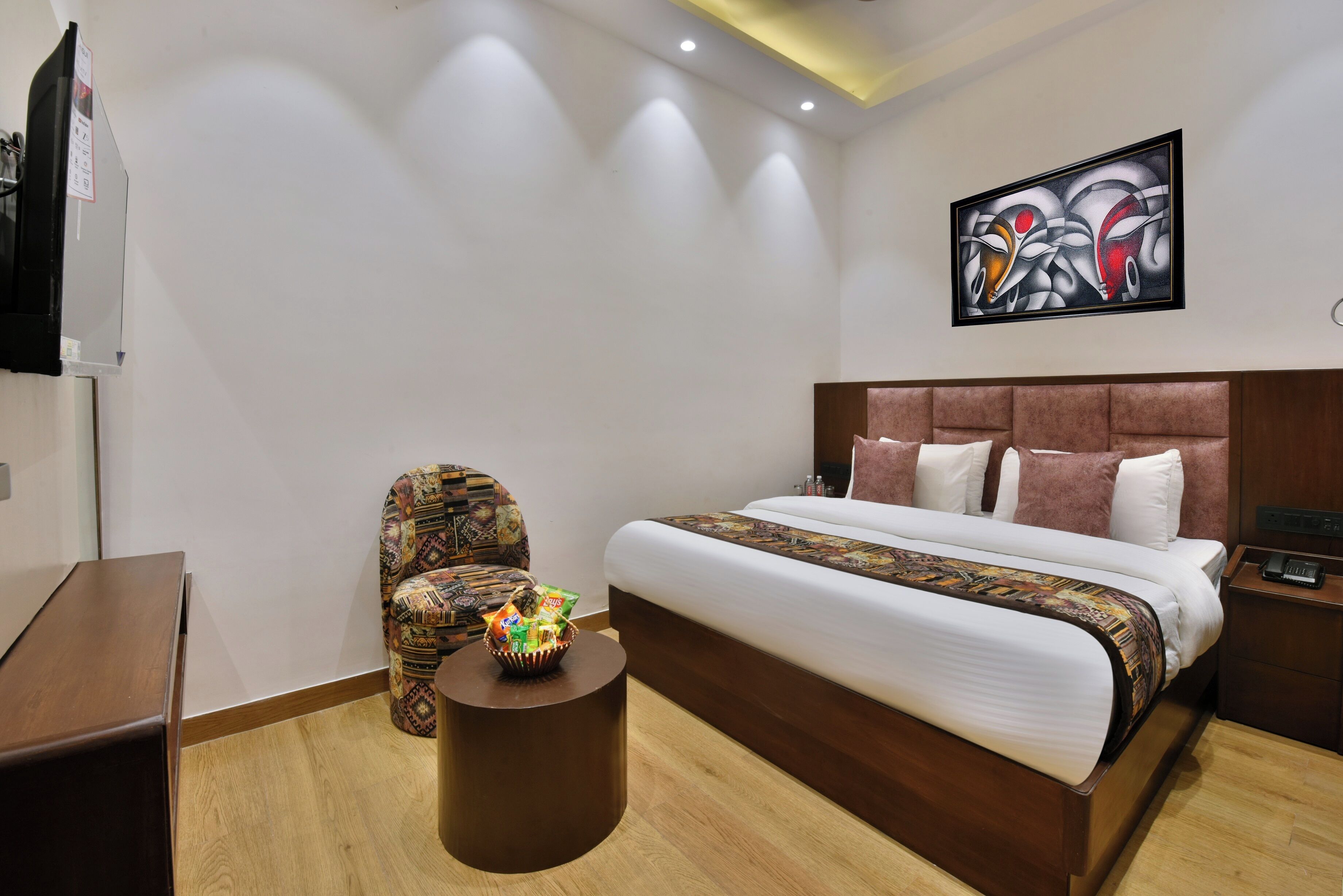 A hotel room with a bed, a chair, a small table, and a painting on the wall.