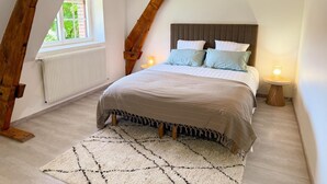 Quarto com teto inclinado, uma cama com cabeceira, uma janela e um radiador.