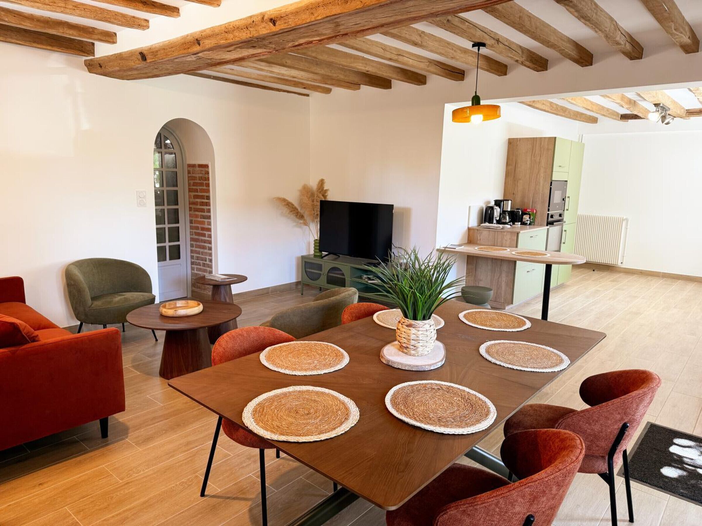 Ein modernes Wohnzimmer mit einem Holzespeisetisch, roten und grünen Stühlen, einem Fernseher und einer Küchenzeile.