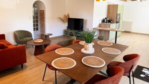Uma sala de estar moderna com uma mesa de jantar de madeira, cadeiras vermelhas e verdes, uma televisão e uma área de cozinha.