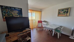 Ein Wohnzimmer mit Flachbildfernseher, einem roten Sessel, einem kleinen Tisch und einem Bild an der Wand.