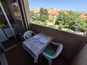 A balcony with a table set for two, chairs, and a view of buildings and trees. - Charming apartment, private parking - 2 guests (Collioure)