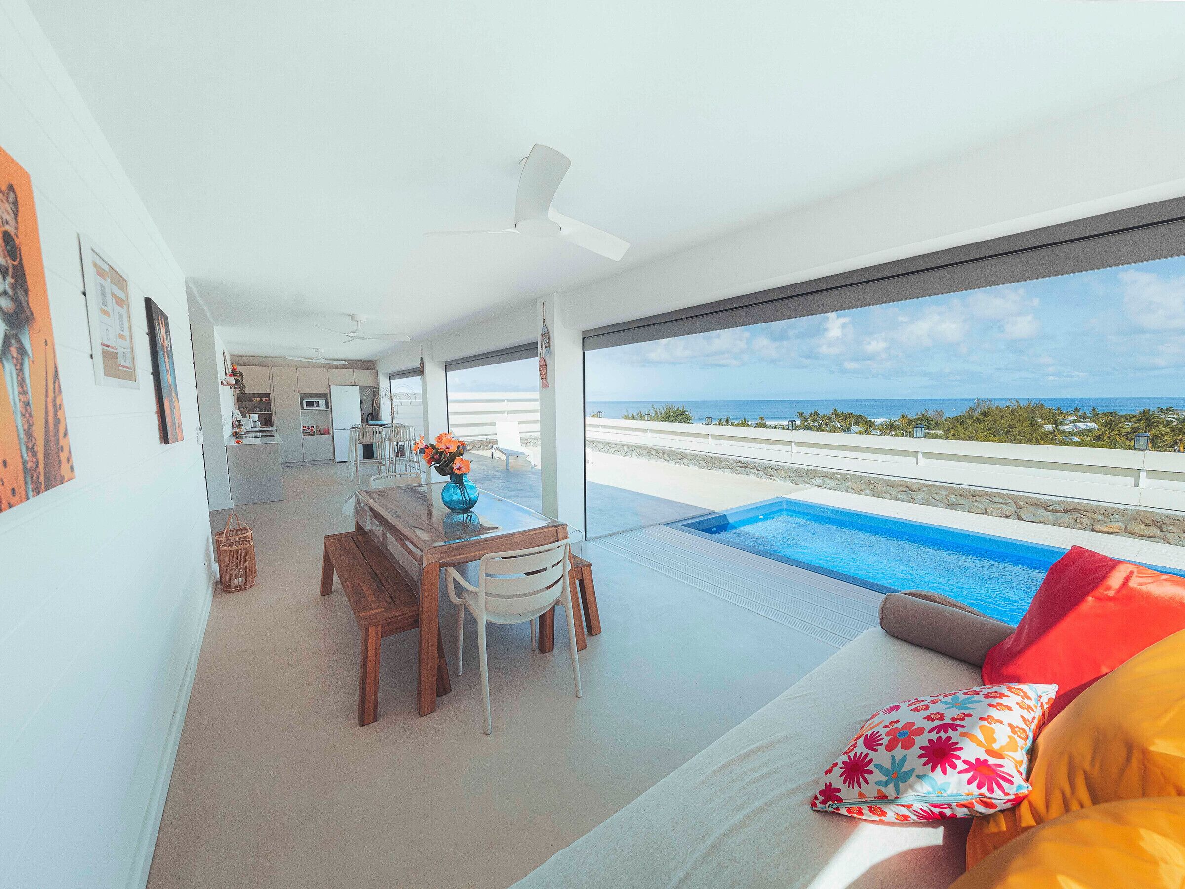 Un intérieur moderne comprenant un coin repas, une piscine et une vue sur l’océan.