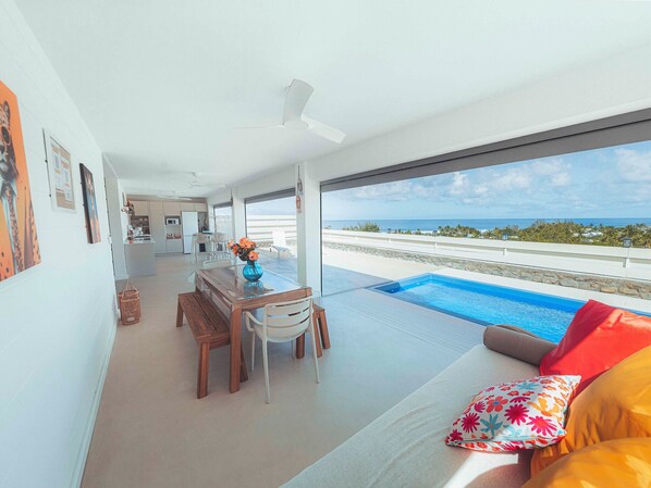 Un interior moderno con comedor, piscina y vista al océano.