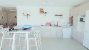 A modern kitchen with white cabinetry, a dining area with white chairs, and a small refrigerator. - Villa for 10 guests, private pool and AC (Saint-Paul)