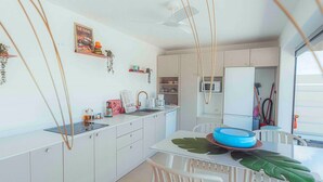 A modern kitchen with white cabinets, a dining table with chairs, a ceiling fan, and a view of the outside. - Villa for 10 guests, private pool and AC (Saint-Paul)