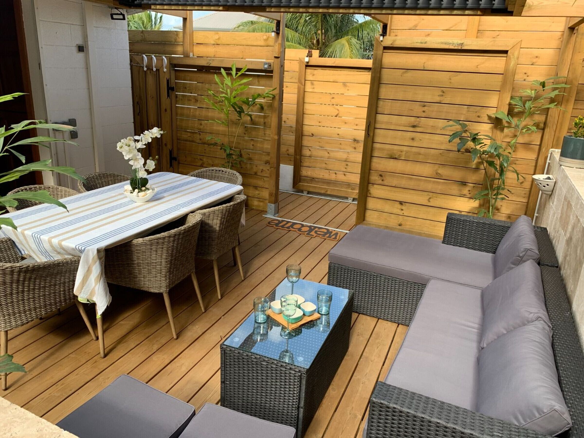 An outdoor patio with a dining table, wicker chairs, a sofa, and a small table with drinks.