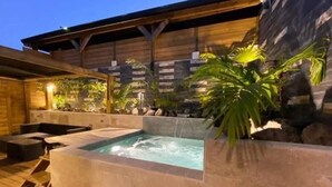 Ein Whirlpoolbereich mit Steinwänden, Holzterrasse und Kübelpflanzen.
