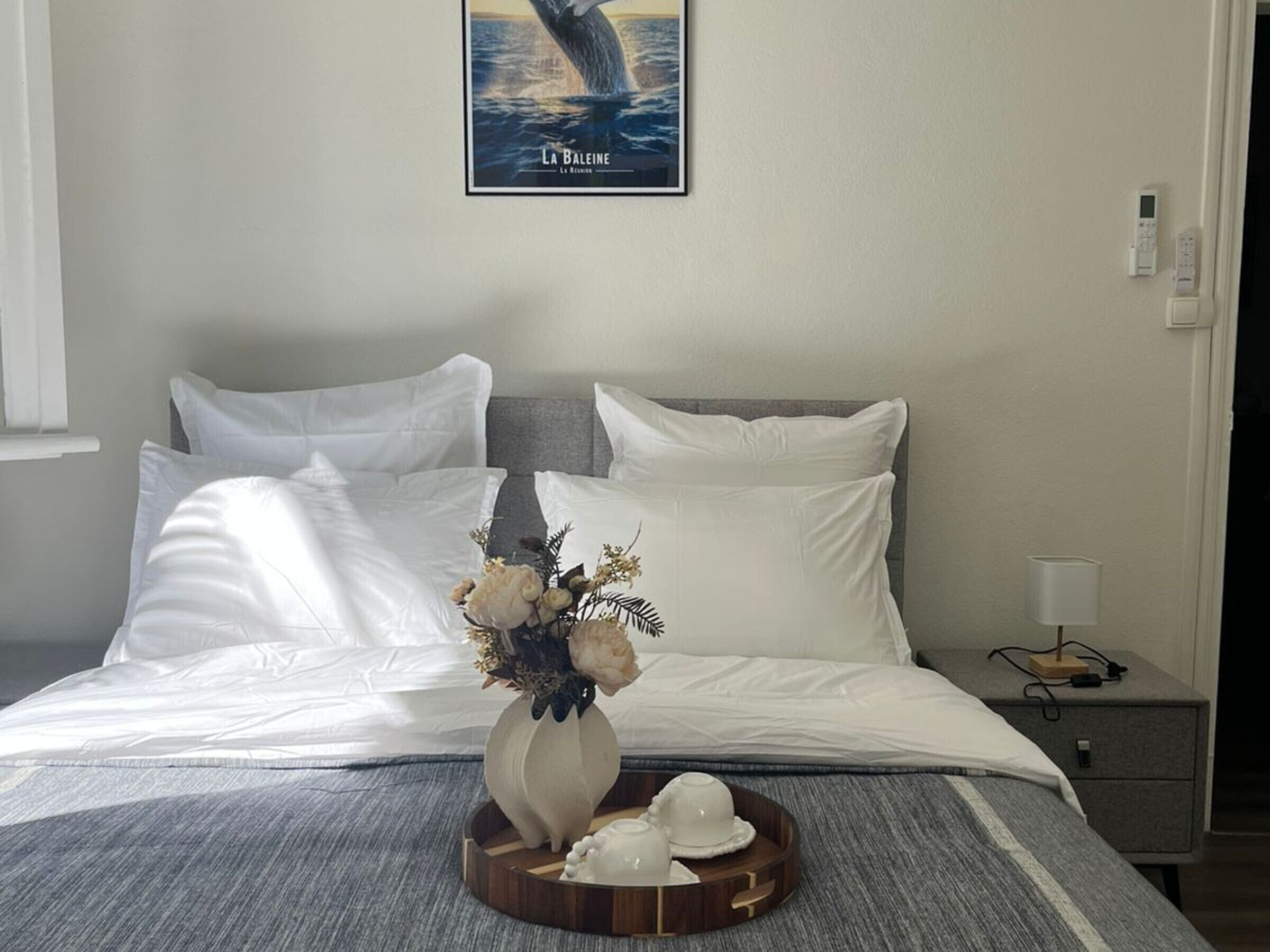 A neatly made bed with white linens, a vase with flowers, and a tray with teacups.