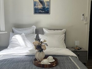 A neatly made bed with white linens, a vase with flowers, and a tray with teacups.