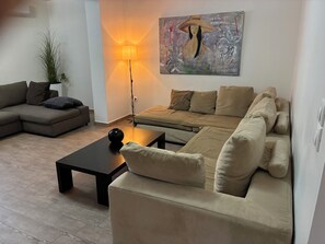 A living room with a sectional sofa, a small coffee table, a floor lamp, and a painting on the wall. - Fabulous 2-bedroom apartment with AC in Kalivia Thorikou (Kalivia Thorikou)