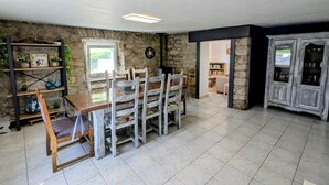 Un coin repas avec un mur en pierre, une table en bois et des chaises. On y trouve une bibliothèque agrémentée d’objets décoratifs et une fenêtre qui laisse entrer la lumière naturelle.