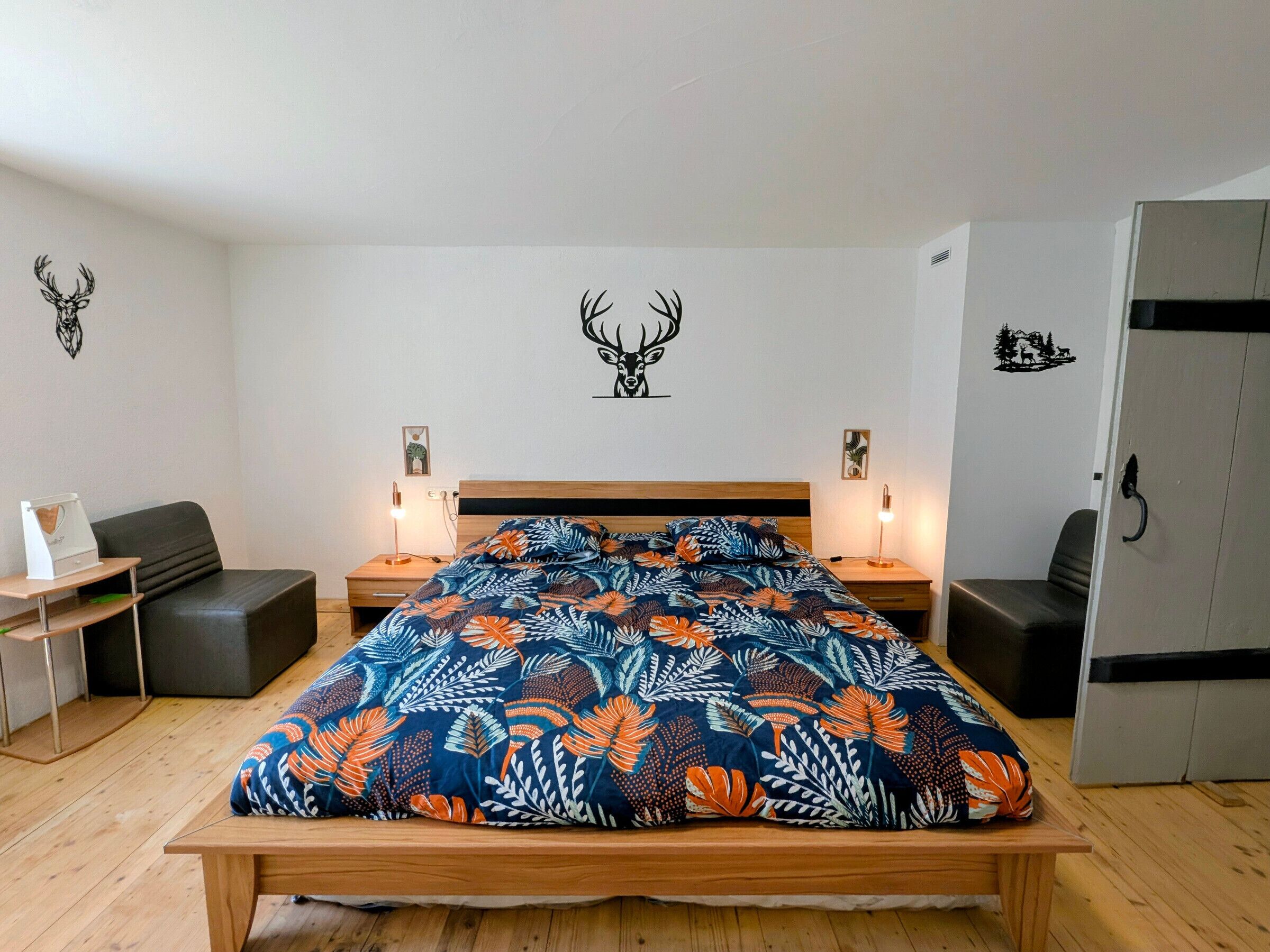 A bedroom with a wooden bed, two bedside tables with lamps, a desk, a chair, and a wardrobe.
