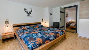 Une chambre à coucher avec un lit en bois, une table de chevet, une chaise et une porte donnant sur une autre pièce.