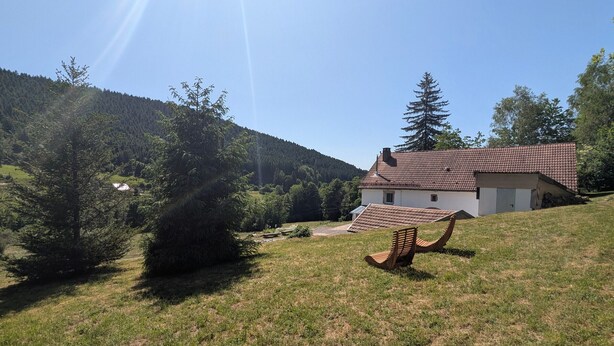 Une maison avec un toit en pente, entourée d’une pelouse et d’arbres.