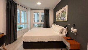 Ein modernes Schlafzimmer mit einem großen Bett, einem Schreibtisch und einem Fenster mit Vorhängen.