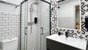 Ein Badezimmer mit einer Duschkabine aus Glas, weißen Fliesen im U-Bahn-Stil, einer schwarz-weißen Wandgestaltung und einem weißen Waschbecken mit dunkler Arbeitsplatte.