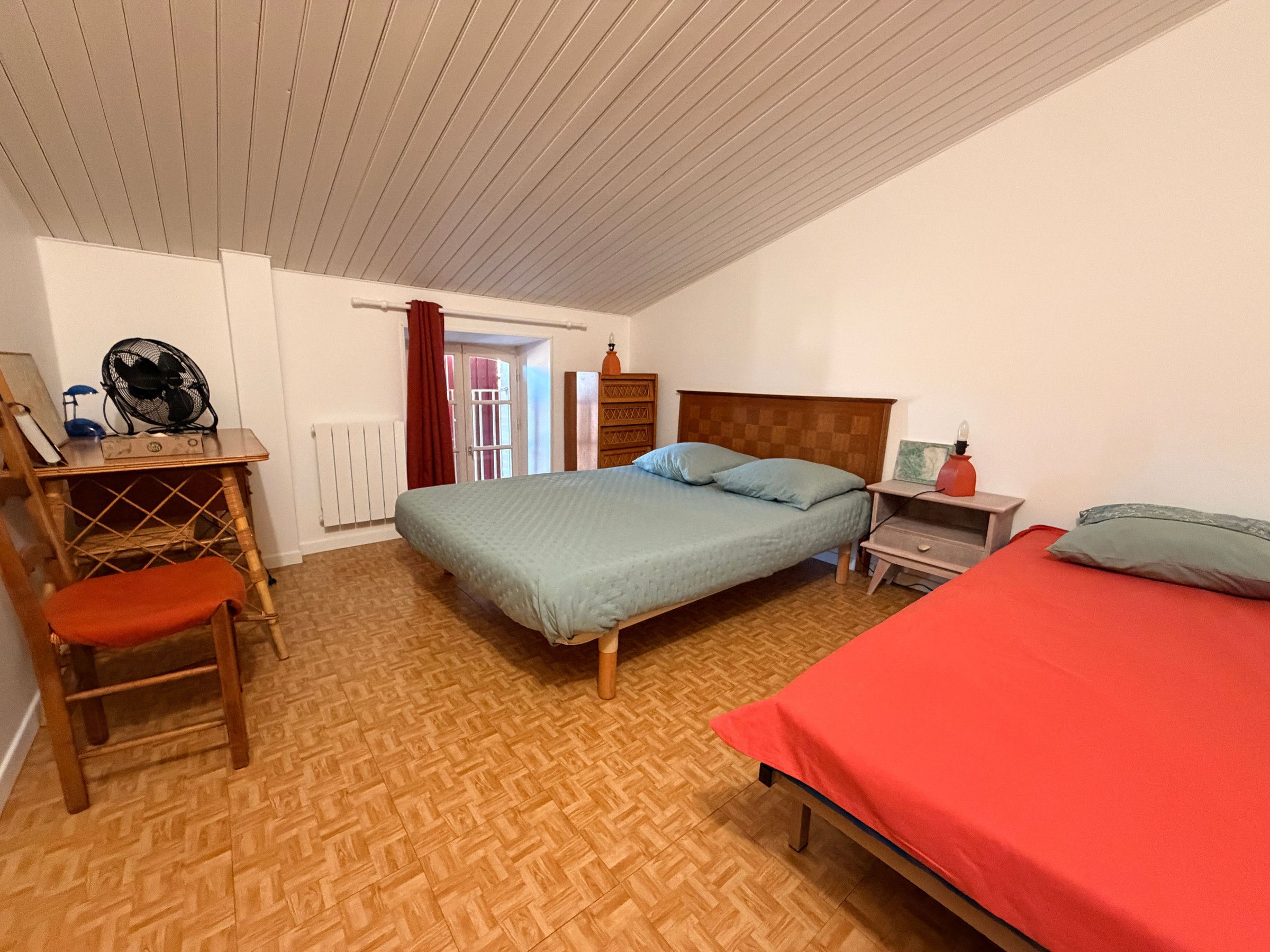 Un dormitorio con cama, escritorio, silla, mesita de noche y ventilador.