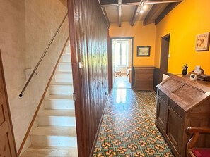 Um corredor com escadas de madeira, piso estampado e um armário de madeira com uma tela pequena.
