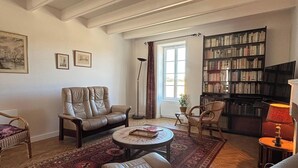 Ein Wohnzimmer mit einer Couch, Sesseln, einem Couchtisch, einem Bücherregal und einem Fernseher.