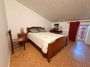 A bedroom with a wooden bed, a nightstand, a chair, a desk, and a window with curtains. - Spacious house near Marais Poitevin (Le Langon)