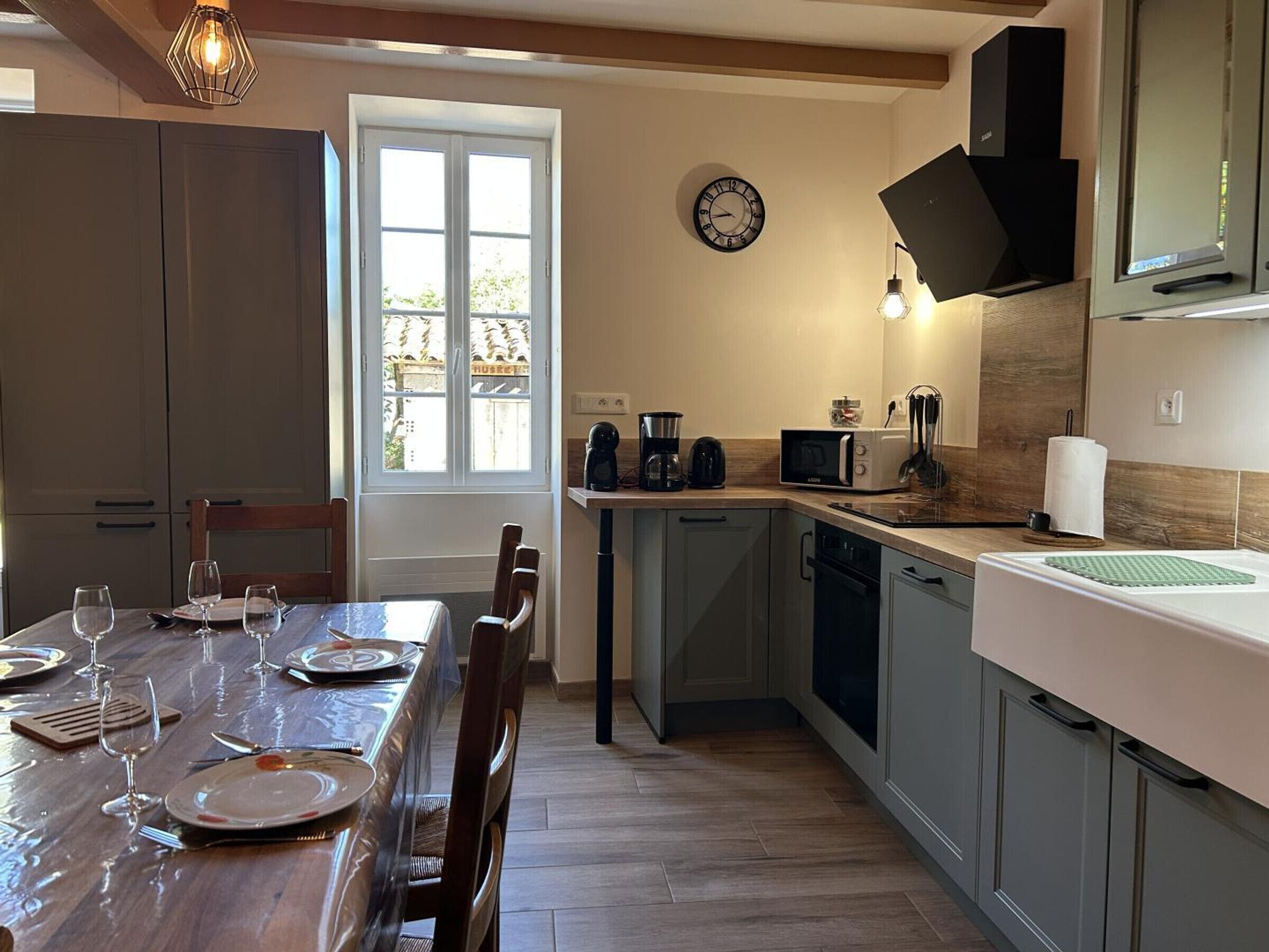 Una cocina con una mesa de comedor para cuatro personas, una cafetera, un microondas y un reloj en la pared.
