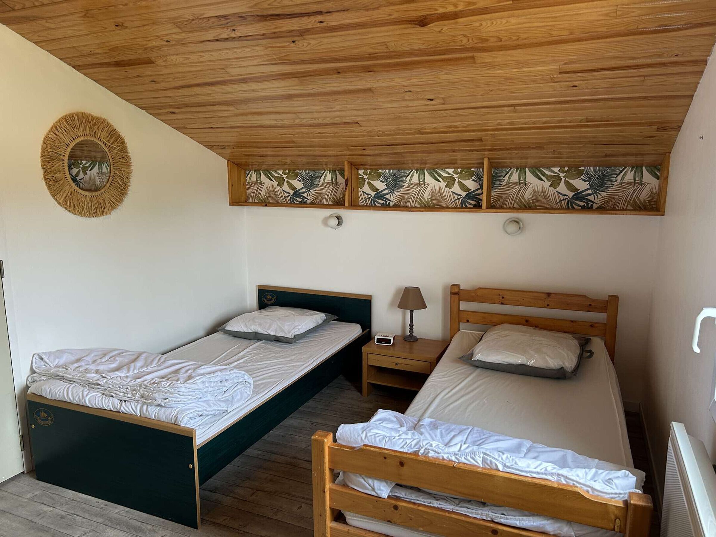 A room with two single beds, a nightstand with a lamp, and a wall-mounted mirror.
