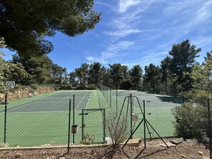 Een tennisbaan omringd door bomen en een basketbalveld.