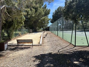 Una cancha de tenis con red, rodeada de árboles y un sendero de grava.