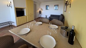 Una zona de menjador amb una taula preparada per a quatre persones, una televisió, un sofà i una làmpada.