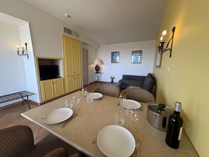 A dining area with a table set for four, a television, a sofa, and a lamp. - Apartment with AC, sea view - 6 guests (Saint-Cyr-sur-Mer)