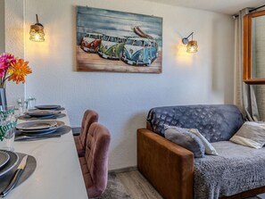 Ein Essbereich mit einem Tisch für vier Personen, einer Couch und einem Bild von Oldtimern an der Wand.