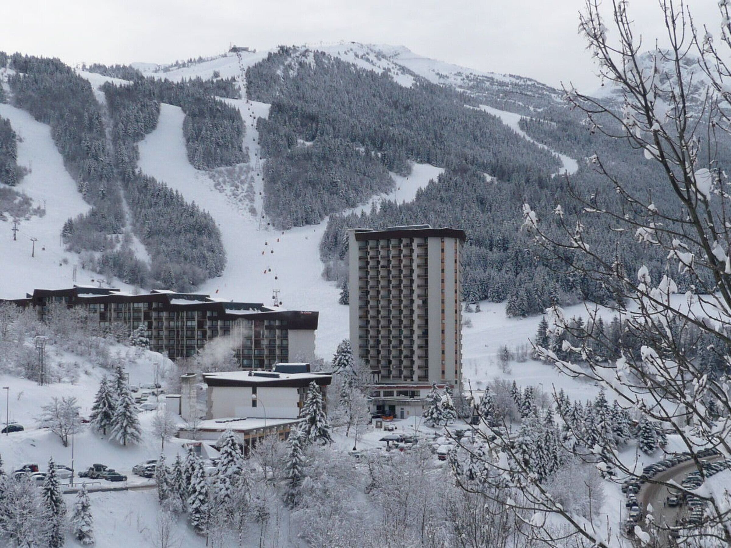 Estância de esqui com um edifício alto, vários edifícios menores e uma montanha nevada ao fundo.