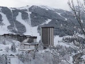 Ein Skigebiet mit einem hohen Gebäude, mehreren kleineren Bauten und einem verschneiten Berg im Hintergrund.