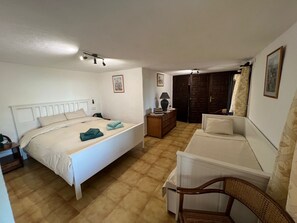 Ein Schlafzimmer mit Bett, Nachttisch, Lampe, Kommode und einem Sessel.