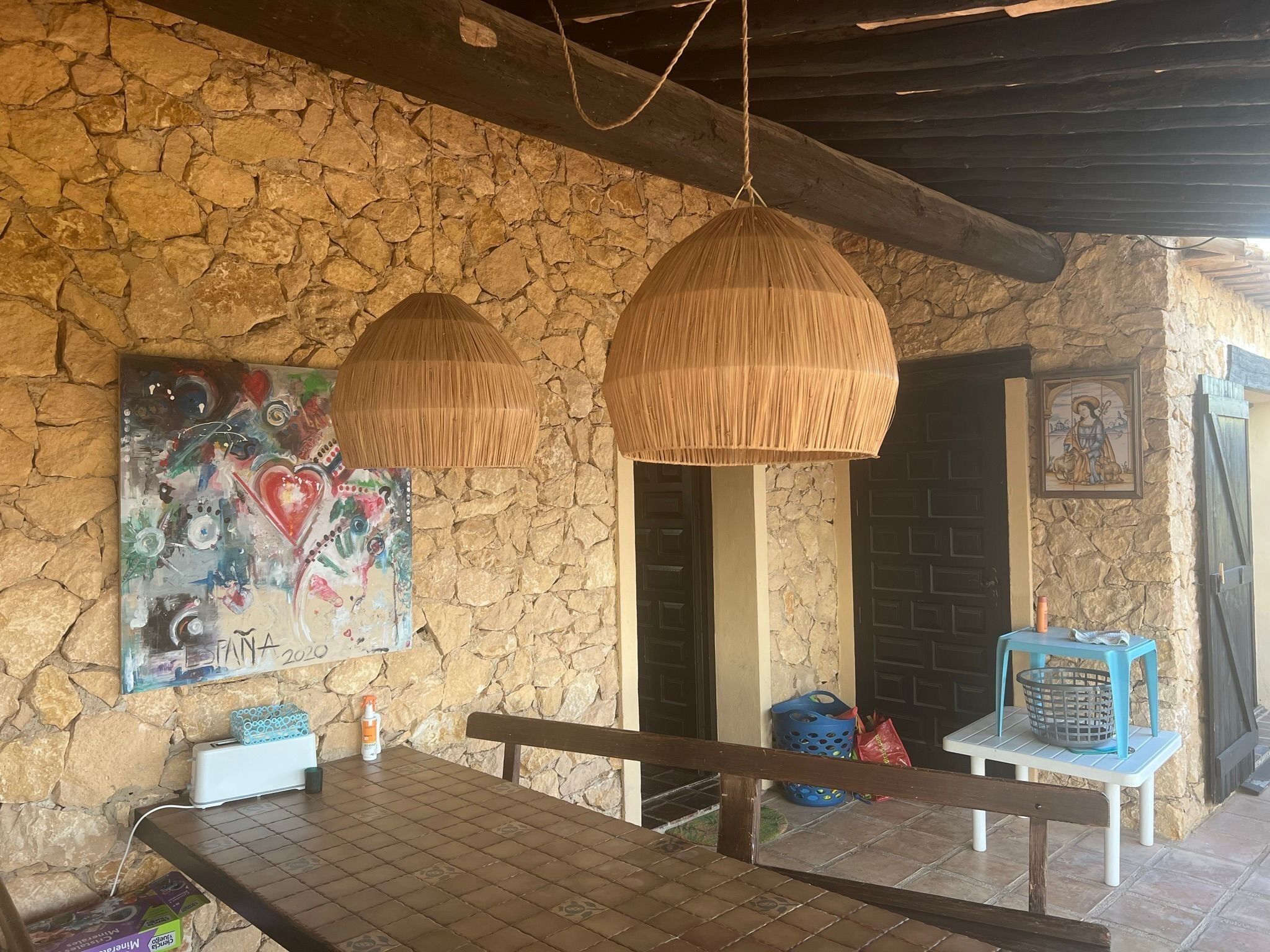 Une pièce aux murs de pierre, avec un banc, une table et deux lampes suspendues.