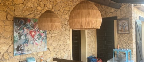 Une pièce aux murs de pierre, avec un banc, une table et deux lampes suspendues.
