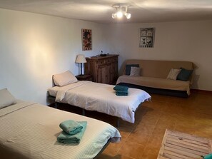 Ein Zimmer mit zwei Betten, einem Holzschrank, einer Couch und einer Deckenleuchte.