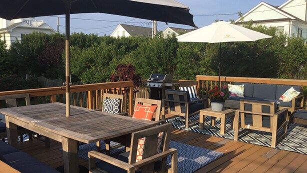 A wooden deck with outdoor furniture, including a table and chairs, and two umbrellas. - Ocean Block.  Amazing 5-bedroom house with AC in charming Spring Lake! (Spring Lake)
