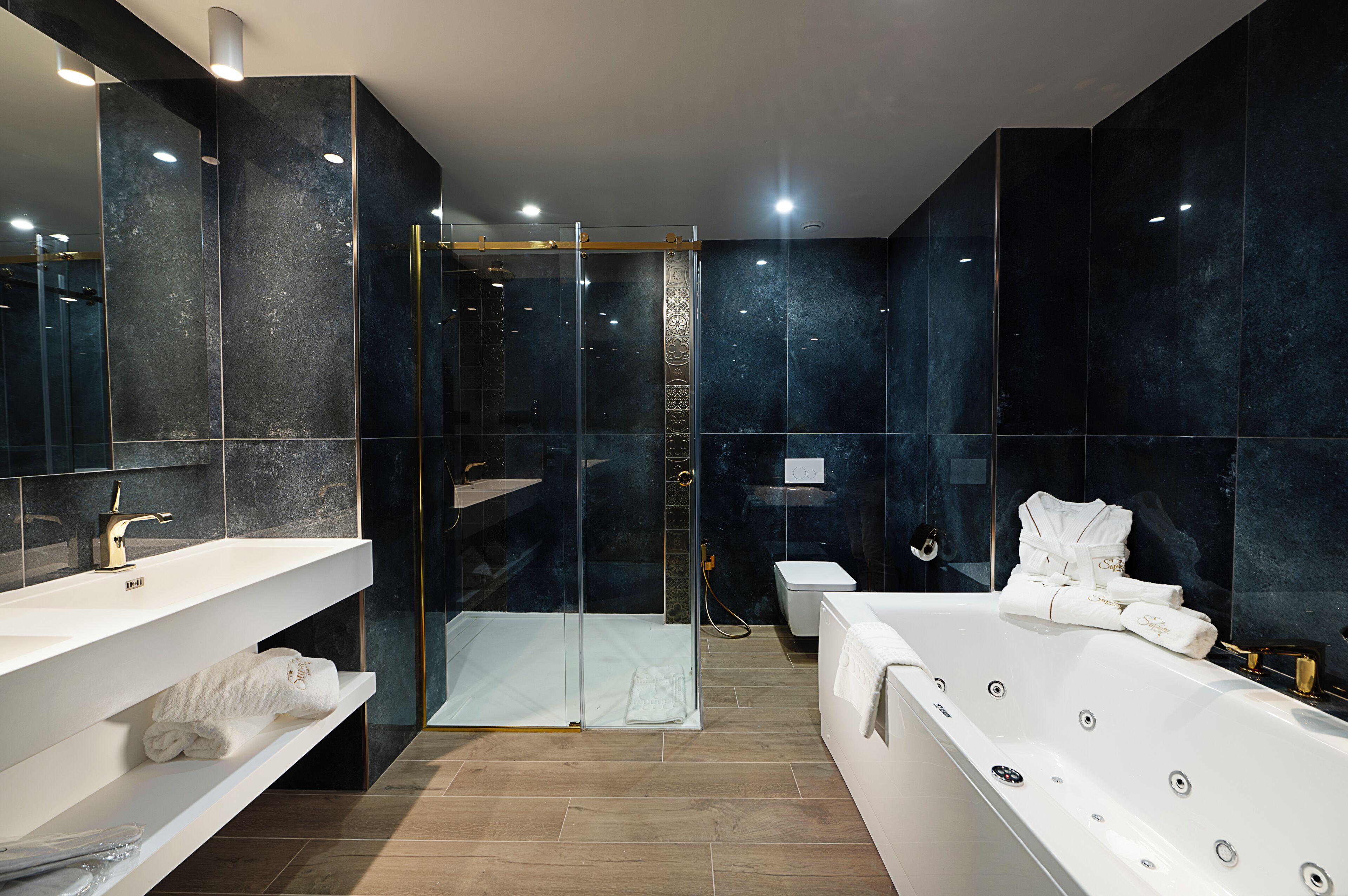 Un baño moderno con ducha de vidrio, una bañera blanca y dos lavamanos con toallas.