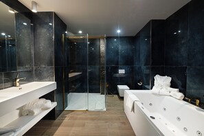 Un baño moderno con ducha de vidrio, una bañera blanca y dos lavamanos con toallas.