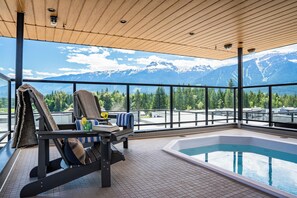 A pool area with a view of snow-capped mountains, a lounge chair, and a small table with a glass and book. - Hot Sauce Hideaway -Revelstoke Vacations (Revelstoke)