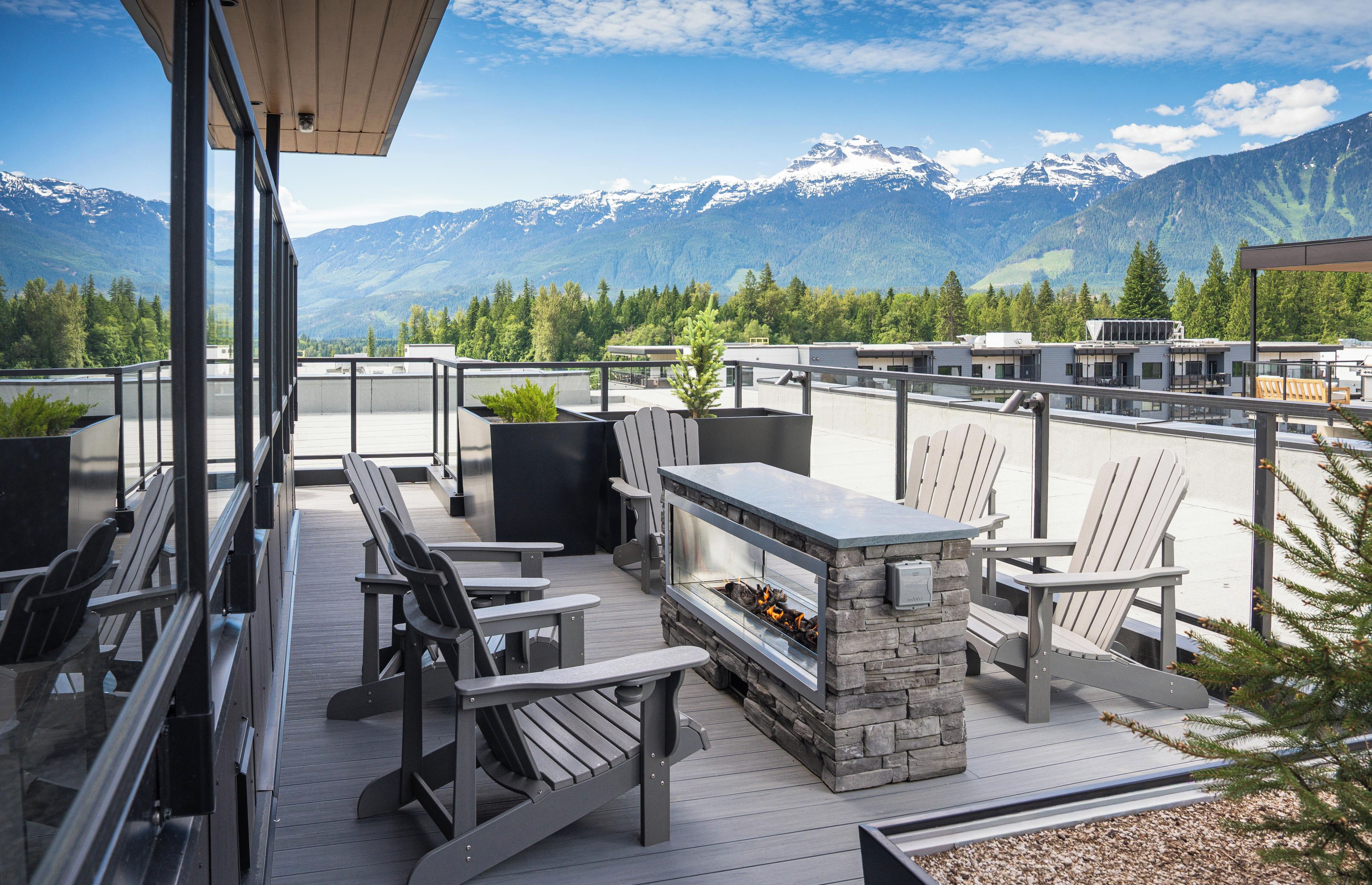 Terraço no telhado com área de estar externa, lareira de pedra e vista para montanhas cobertas de neve.