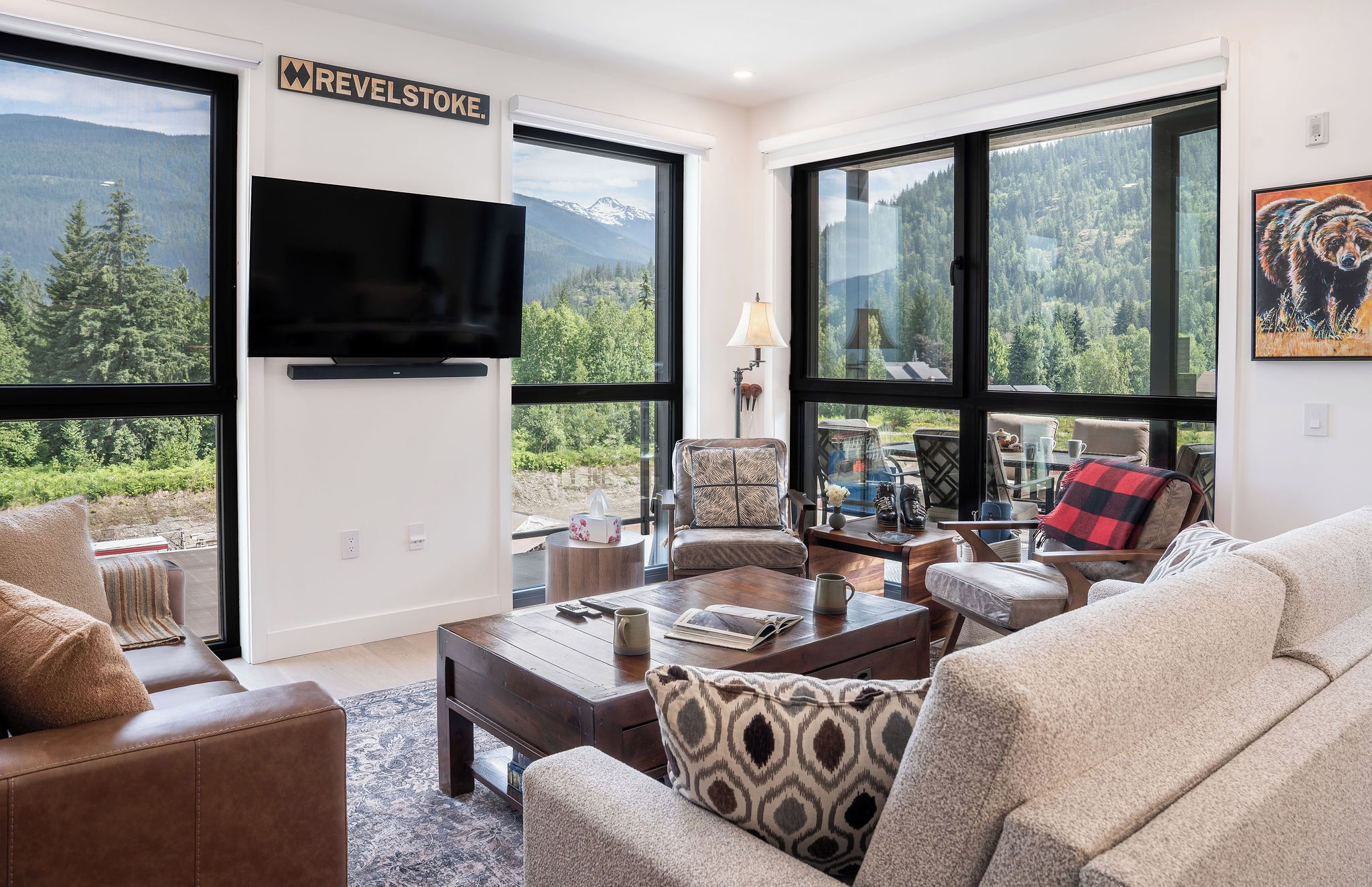 A modern living room with large windows, a flat-screen TV, and a cozy seating area.